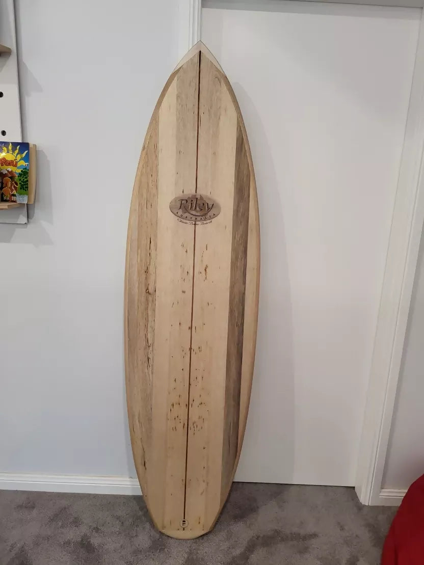 Full deck view of the Riley Hybrid Balsa Secret Weapon surfboard standing indoors