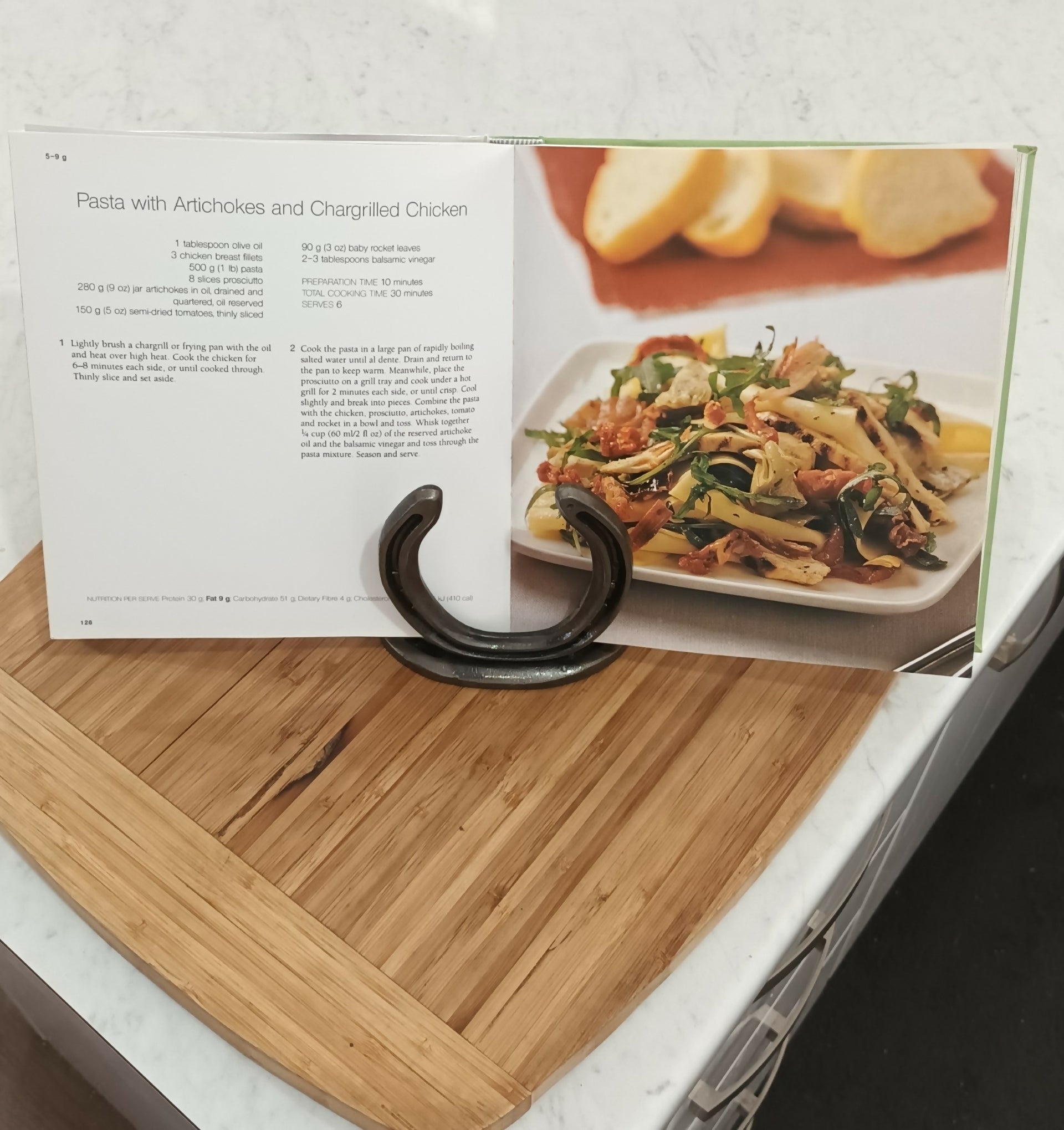 Handmade horseshoe book holder by Noah's Creations displaying an open cookbook on a kitchen bench.