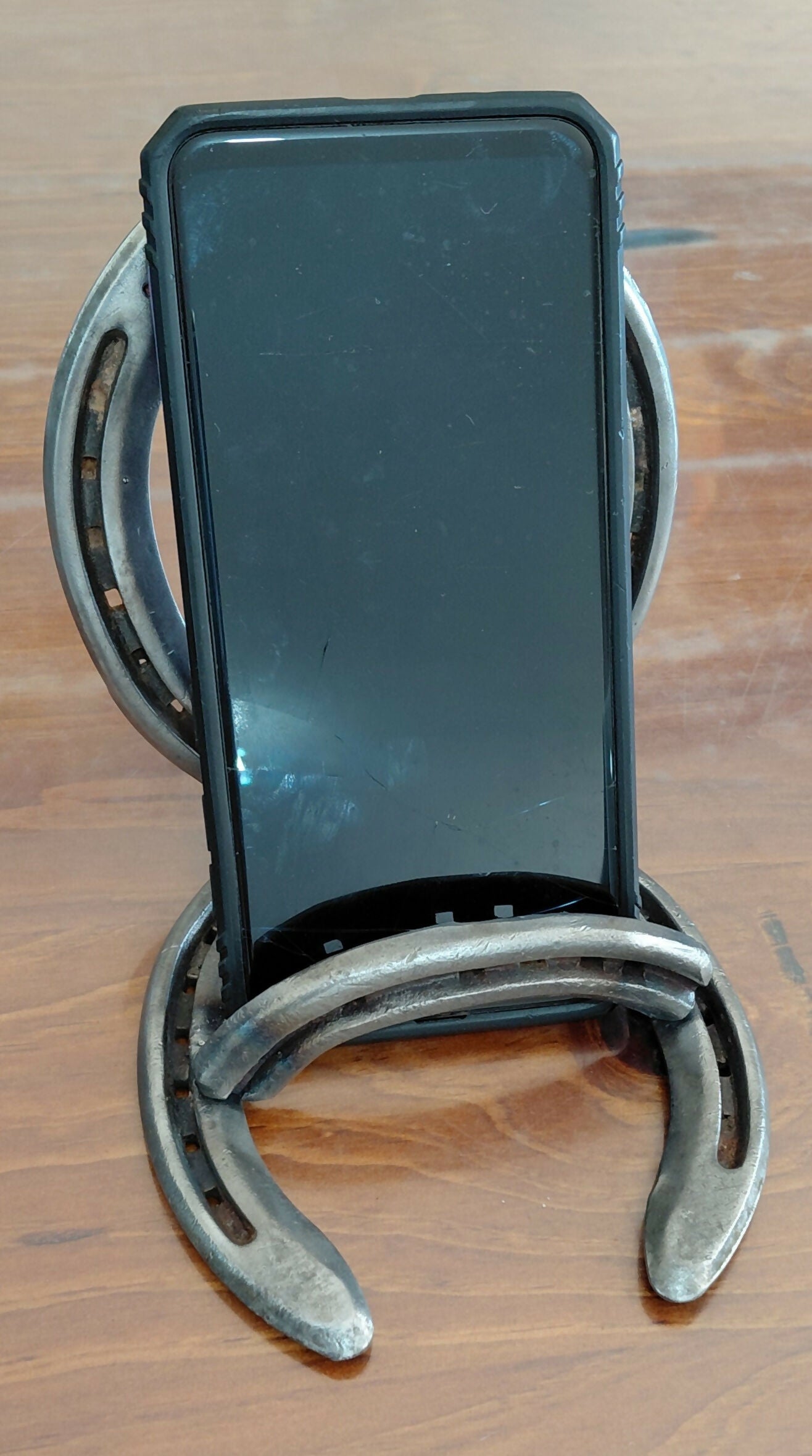 Handmade horseshoe mobile phone and tablet cradle by Noah's Creations holding a smartphone.