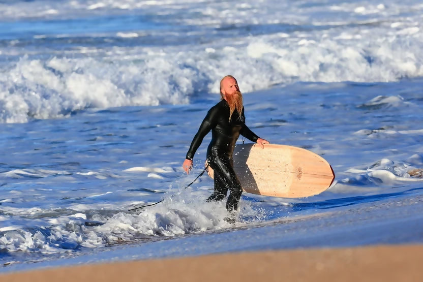 Surfer carrying a Riley Hybrid Balsa Secret Weapon surfboard from the ocean