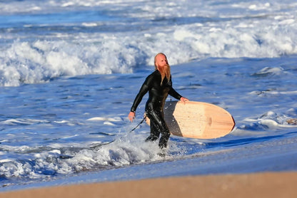 Surfer carrying a Riley Hybrid Balsa Secret Weapon surfboard from the ocean